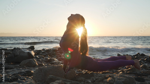 Side view of young caucasian girl practicing yoga at sunset seashore. © Alexander Belinskiy