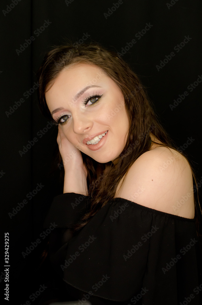 Naklejka premium beautiful brunette young girl happily smiling, hands in hair, looking at camera with fresh make up on black background, studio shot, vertical image