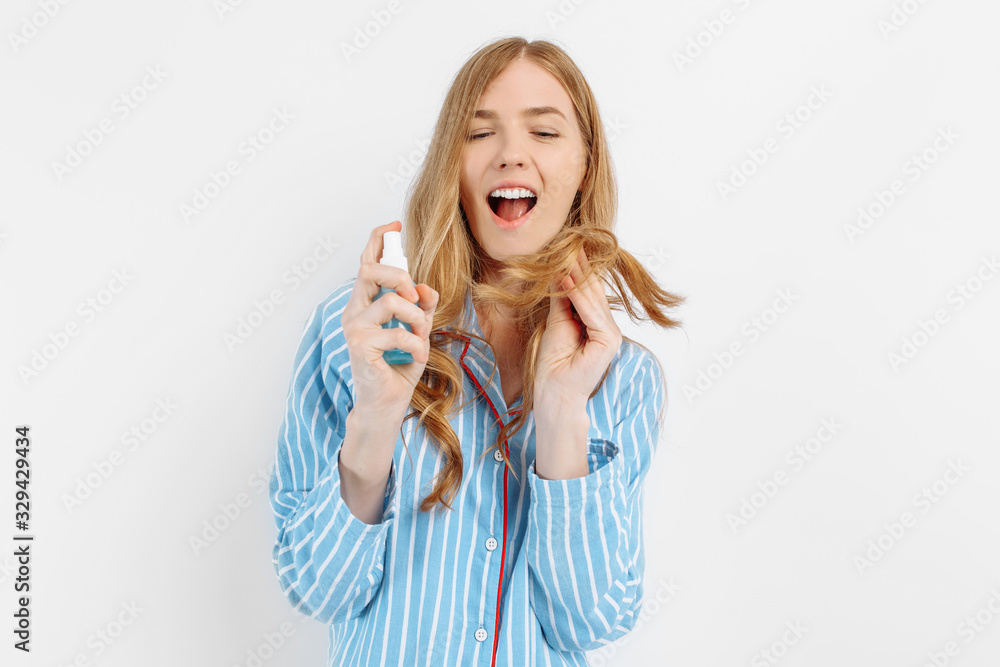 Portrait of happy beautiful young woman in pajamas posing on white background holding hair care bottle Portrait of happy beautiful young woman in pajamas posing on white background holding hair care bottle