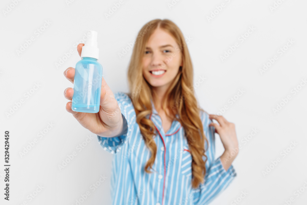Portrait of happy beautiful young woman in pajamas posing on white background holding hair care bottle Portrait of happy beautiful young woman in pajamas posing on white background holding hair care bottle