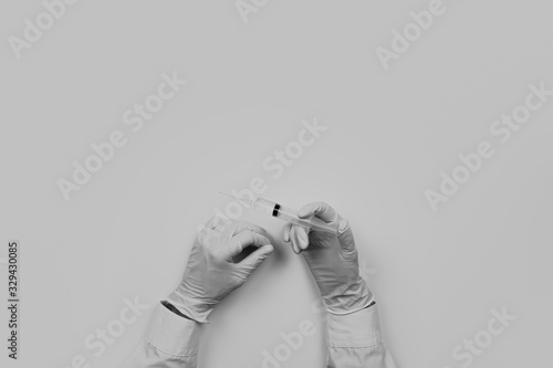 Medical doctor working place flat lay, faded monochrome. Top view of hands of MD holding syringe ready for injection on table with medical utensils