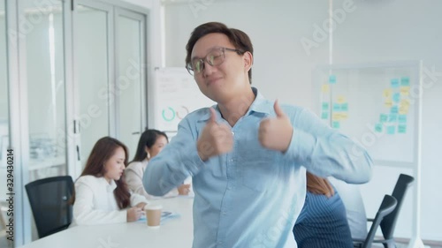 Confident Asian Businessman Showing Thumb up Sign while standing in front of his Colleagues.Male Office Worker Gesturing Like and Agreement Sign by using a finger sign with smiling face. photo