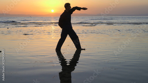 Silhouette of man practicing energy exercises at sunset by the sea