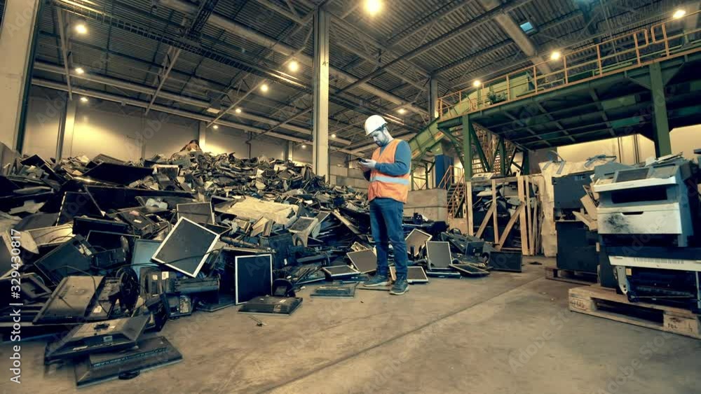 Broken computers are being observed by a male junkyard employee. Garbage, trash, waste recycling factory. Broken computers are being observed by a male junkyard employee. Garbage, trash, waste recycling factory.