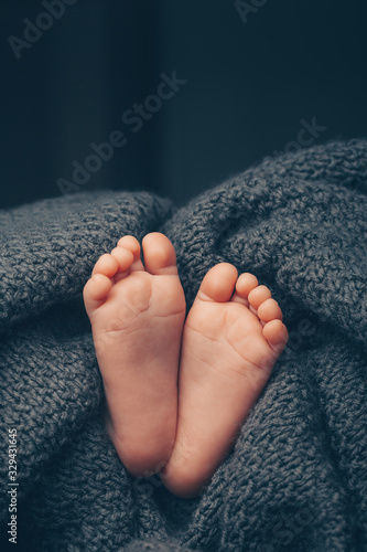 Soft newborn baby feet against a dark grey blanket, closeup