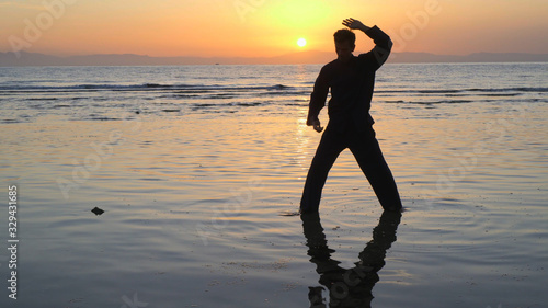 Silhouette of man practicing energy exercises at sunset by the sea
