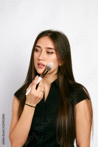 Professional makeup artist poses with the makeup brush and makeup products for advertising on white background.