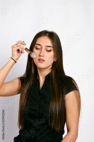 Professional makeup artist poses with the makeup brush and makeup products for advertising on white background.