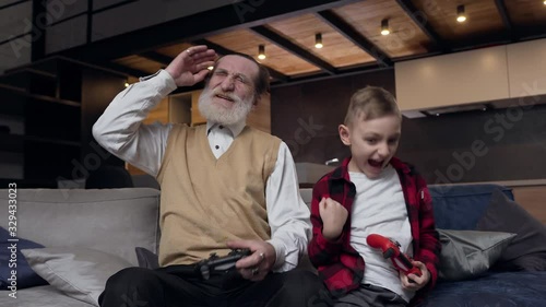 Slow motion of focused attantive mature bearded man and his teen grandson which having fun together at playing video games using joysticks photo