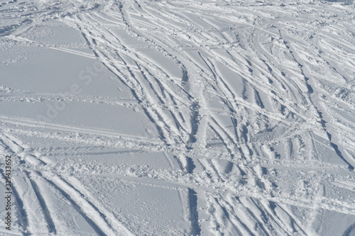skiing slope or ski piste illuminated by direct sun covered by irregular traces  of skis or trajectories in crisp white snow
