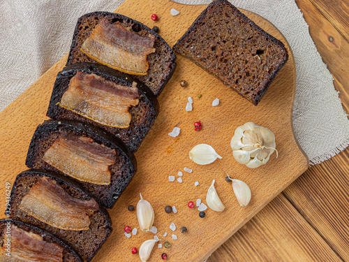 Black bread toasts with bacon on wooden background with garlic and salt