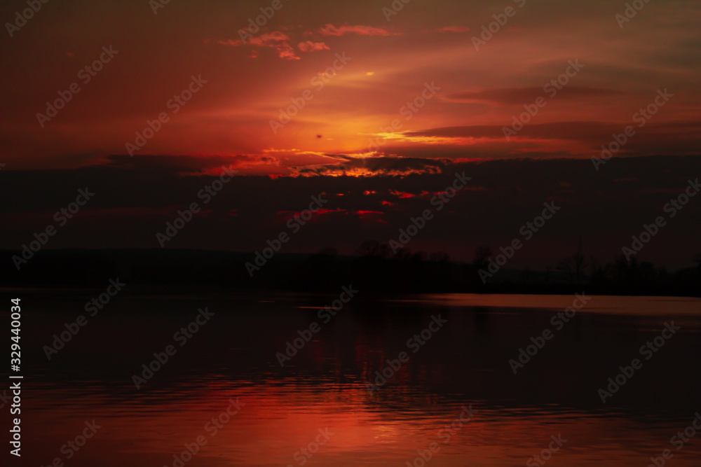 sunset over the river the sun hid behind the clouds a bloody sky in a dark vein
