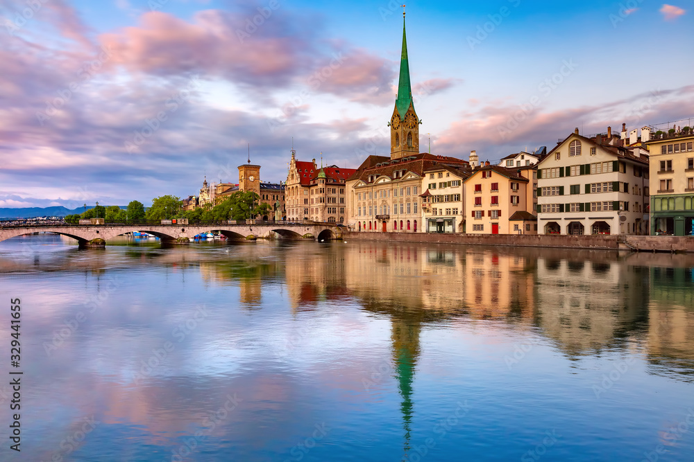 Famous Fraumunster church with its reflections in river Limmat at pink sunrise in Old Town of Zurich, the largest city in Switzerland