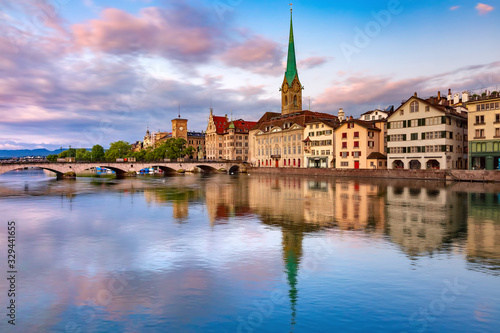 Famous Fraumunster church with its reflections in river Limmat at pink sunrise in Old Town of Zurich, the largest city in Switzerland