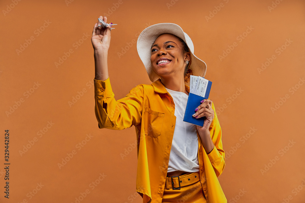 Woman with a smile in a white hat in yellow shirt with a toy airplane with a passport with tickets in hands. Travel concept