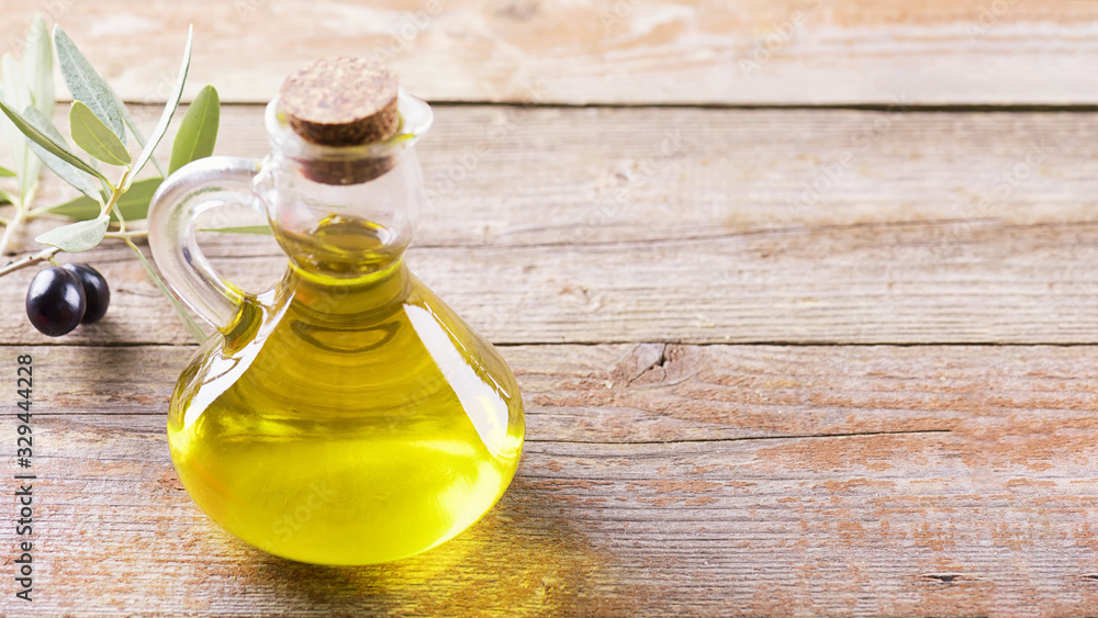 Healthy fats. Bottle of glass full of Extra Virgin Olive Oil made in Puglia, Salento on a wooden table with olive branch Healthy fats. Bottle of glass full of Extra Virgin Olive Oil made in Puglia, Salento on a wooden table with olive branch