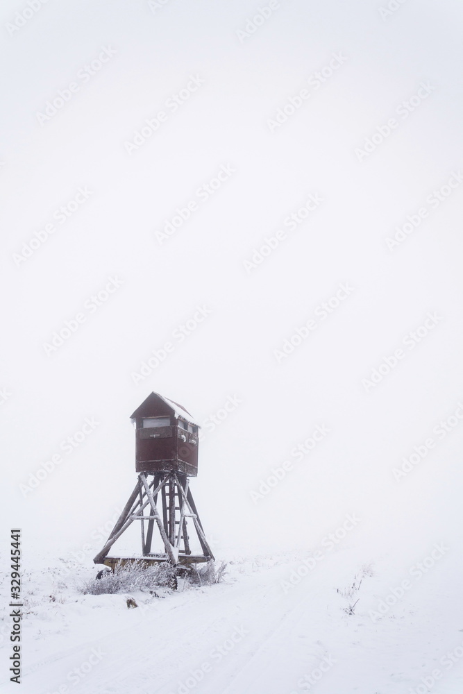 Deer stand, wooden hunters high seat hide on snow covered field, winter foggy day Deer stand, wooden hunters high seat hide on snow covered field, winter foggy day