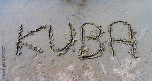 Imię męskie "Kuba" napisane na piasku na plaży. Słowo Kuba oznacza też nazwę kraju - Kuba. Napis na piasku, zrobiony patykiem.