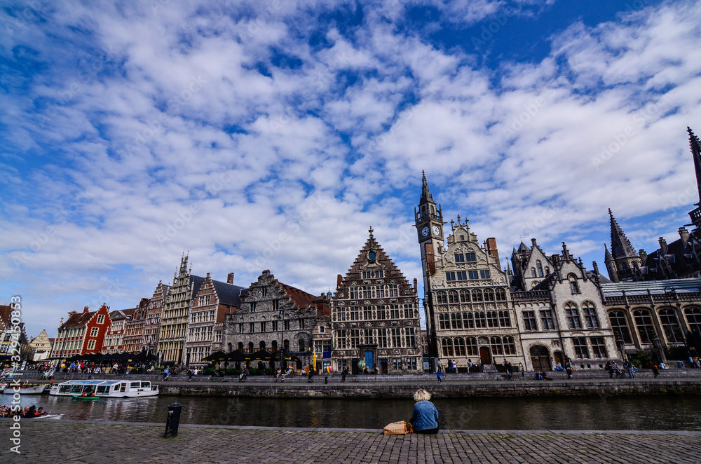 Ghent, Belgium, August 2019. Breathtaking cityscape: from the St. Michael bridge along the Graslei canal. One of the most beautiful postcards in the city. A lady stopped for a break, next to her bags.
