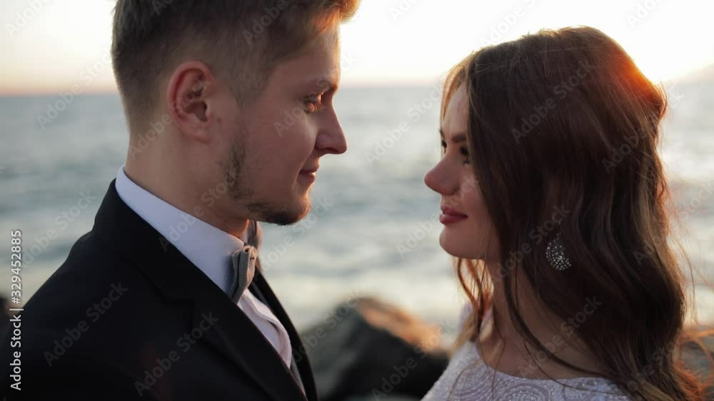 close up portrait of Young couple in love newlyweds.Bride in white wedding dress aganist sea waves, rocks and sunset close up portrait of Young couple in love newlyweds.Bride in white wedding dress aganist sea waves, rocks and sunset