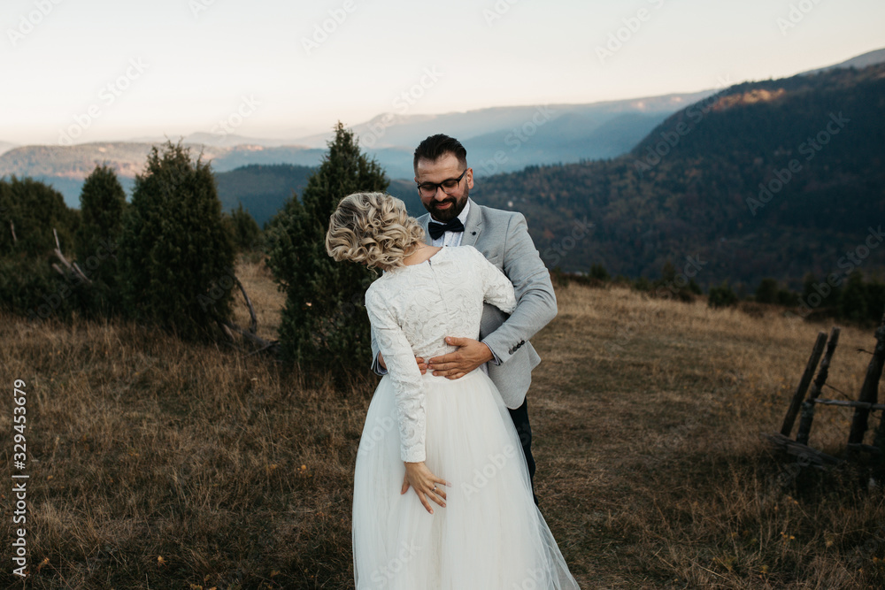 Beautiful couple having a romantic moment on their weeding day, in mountains at sunset. Bride is in a white wedding dress with a bouquet of sunflowers in hand, groom in a suit. Playing together. Beautiful couple having a romantic moment on their weeding day, in mountains at sunset. Bride is in a white wedding dress with a bouquet of sunflowers in hand, groom in a suit. Playing together.