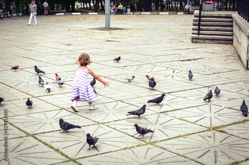 A little girl in a dress runs after the birds.