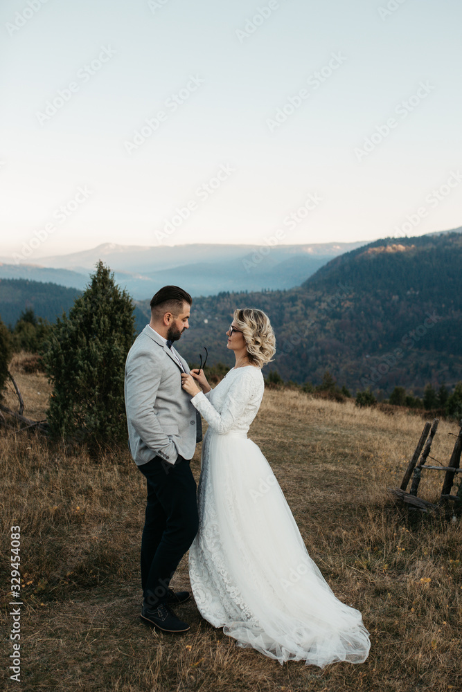 Beautiful couple having a romantic moment on their weeding day, in mountain, sunset.She is in a white wedding dress with a bouquet of sunflowers in hand,groom in a suit. Groom holds bride in his hands Beautiful couple having a romantic moment on their weeding day, in mountain, sunset.She is in a white wedding dress with a bouquet of sunflowers in hand,groom in a suit. Groom holds bride in his hands