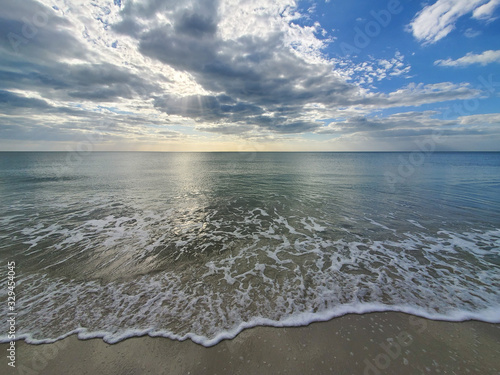 Abstract seascape panoramic background - late afternoon. Calm seas/ocean in the bottom of the frame. Minimalistic simple background image, blue and yellow colors, clouds and sky