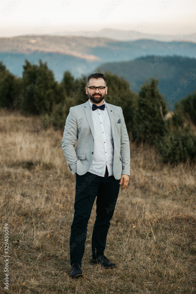 Beautiful elegant groom in wedding suit with long sleeves. Handsome man in tux. Portrait of man wearing glasses in nature. 