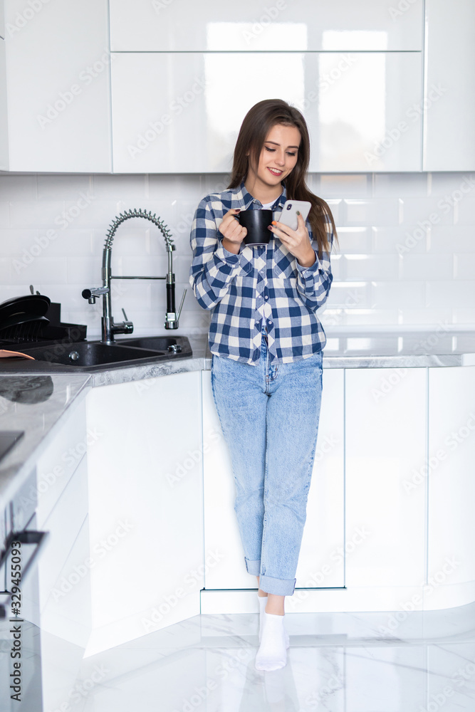 Young woman with her mobile phone and a cup of coffee in the kitchen Young woman with her mobile phone and a cup of coffee in the kitchen