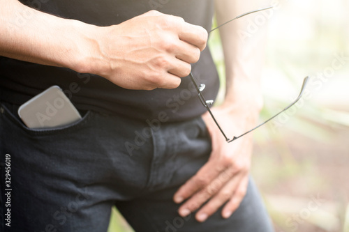 man holding glasses in hand and smart phone in pants pocket