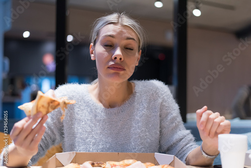 Beautiful woman eating pizza and drinking cola while sitting inside expres restaurant late at night.