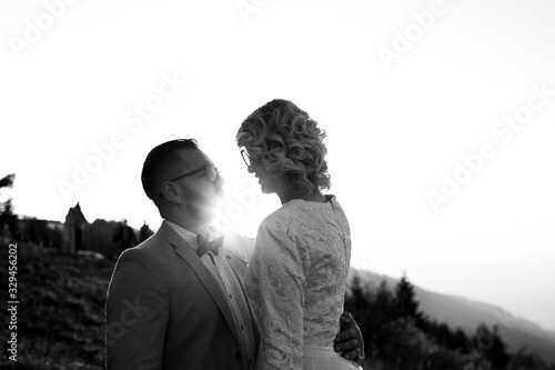  Beautiful couple having a romantic moment on their weeding day, in mountain, sunset.She is in a white wedding dress with a bouquet of sunflowers in hand,groom in a suit. Groom holds bride in his han