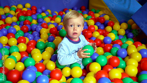 Dziecko wśród kolorowych kulek na placu zabaw w bawialni, chłopiec bawi się kulkami, dziecięce zabawy wśród plastikowych kulek