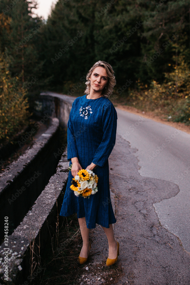 Portrait of Beautiful elegant bride in blue wedding dress with mid length skirt and long sleeves. Pretty girl in white. Nature, with road, sunset time.