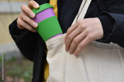 Female hands holding reusable coffee cup putting into a bag outdoors.