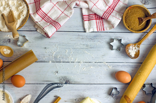 Culinary background baking. Flat lay composition with raw eggs, flour, butter, cake baking dishes, rolling pins, napkins, cookie cutters, and other ingredients on light wooden background,copy space