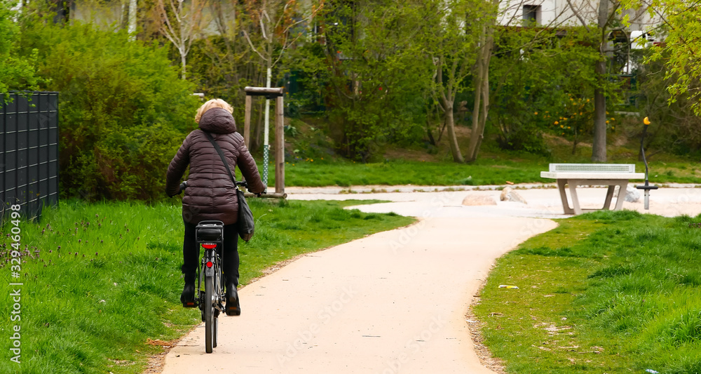 Woman riding her bike in the park. Adult woman in a jacket on a sunny spring day driving to work or school with the bike to have a healthy lifestyle. Woman riding her bike in the park. Adult woman in a jacket on a sunny spring day driving to work or school with the bike to have a healthy lifestyle.