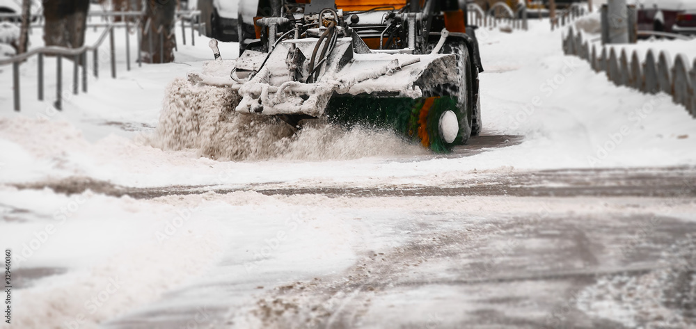 Snow removal equipment. A small snowplow removes the white snow from the streets with a large green brush. Clearing the roads after a snowfall. Snow removal equipment. A small snowplow removes the white snow from the streets with a large green brush. Clearing the roads after a snowfall.