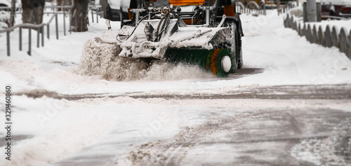 Snow removal equipment. A small snowplow removes the white snow from the streets with a large green brush. Clearing the roads after a snowfall.