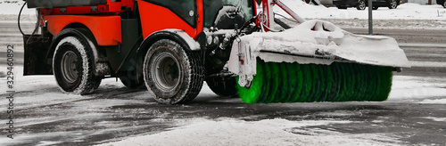 Snow removal equipment. A small snowplow removes the white snow from the streets with a large green brush. Clearing the roads after a snowfall.