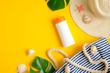 Top view suntan cream bottle, beach bag, female hat and tropical leaves on yellow background. Sun protection on summer vacation concept
