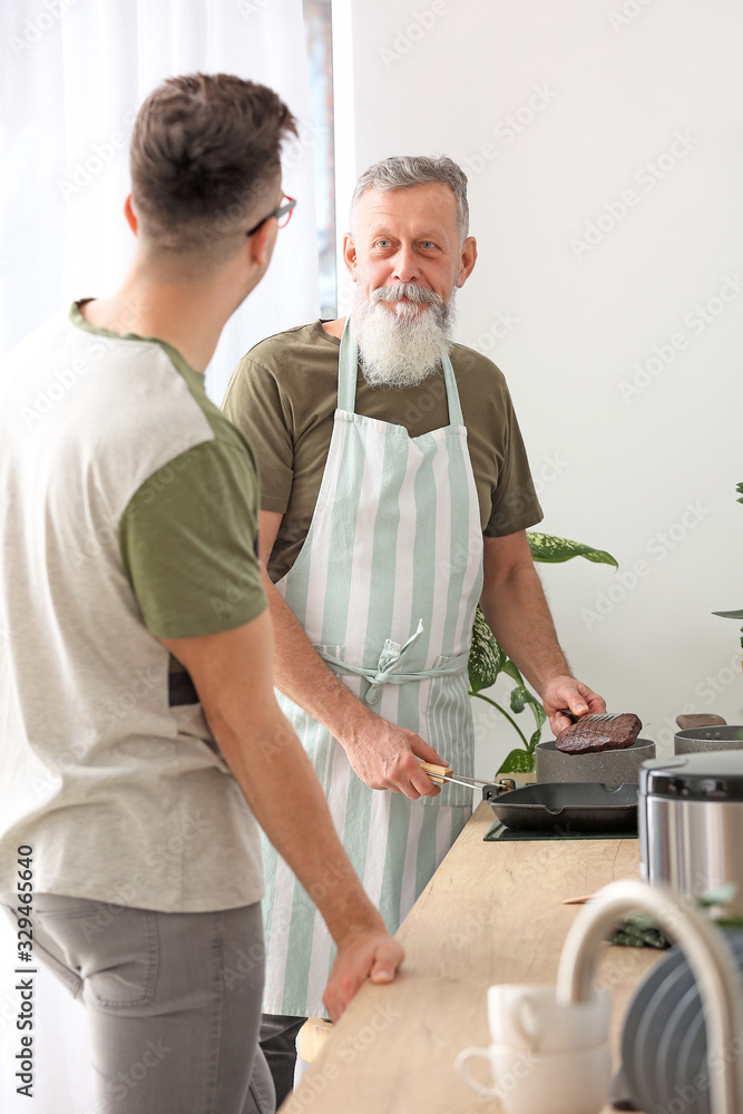 Fototapeta premium Senior man and his adult son cooking together in kitchen