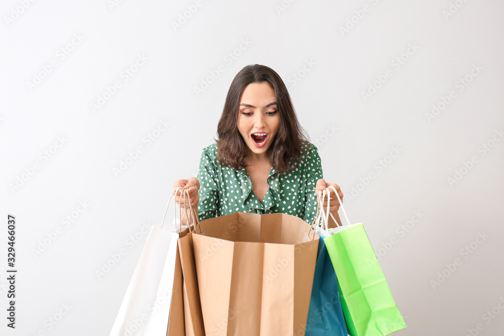 Surprised young woman with shopping bags on light background Surprised young woman with shopping bags on light background