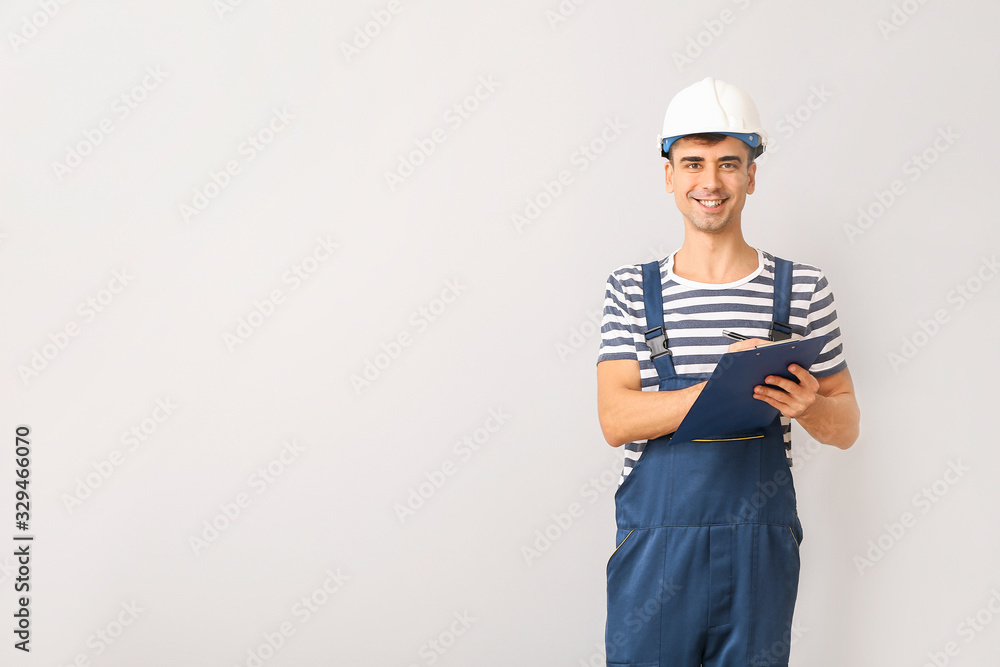 Handsome male worker with clipboard on light background