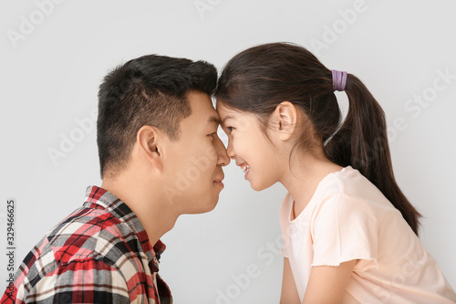 Happy Asian man with his little daughter on light background
