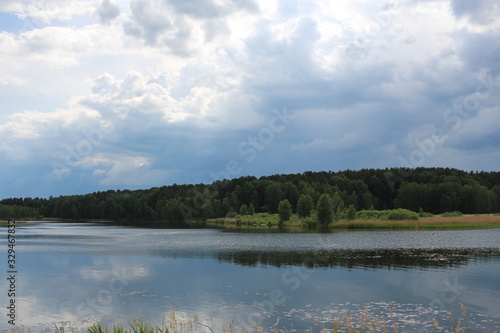 lake pond in the grass in the summer in the forest on the background of a thundercloud river