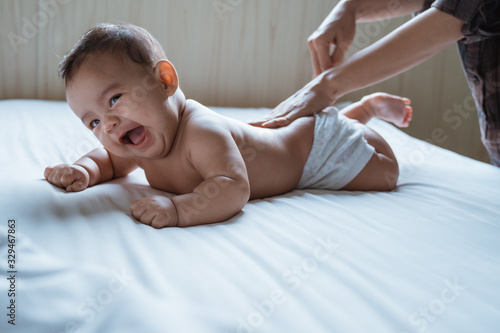 prone baby happy is rubbed his back by his mother while lying in the bedroom photo