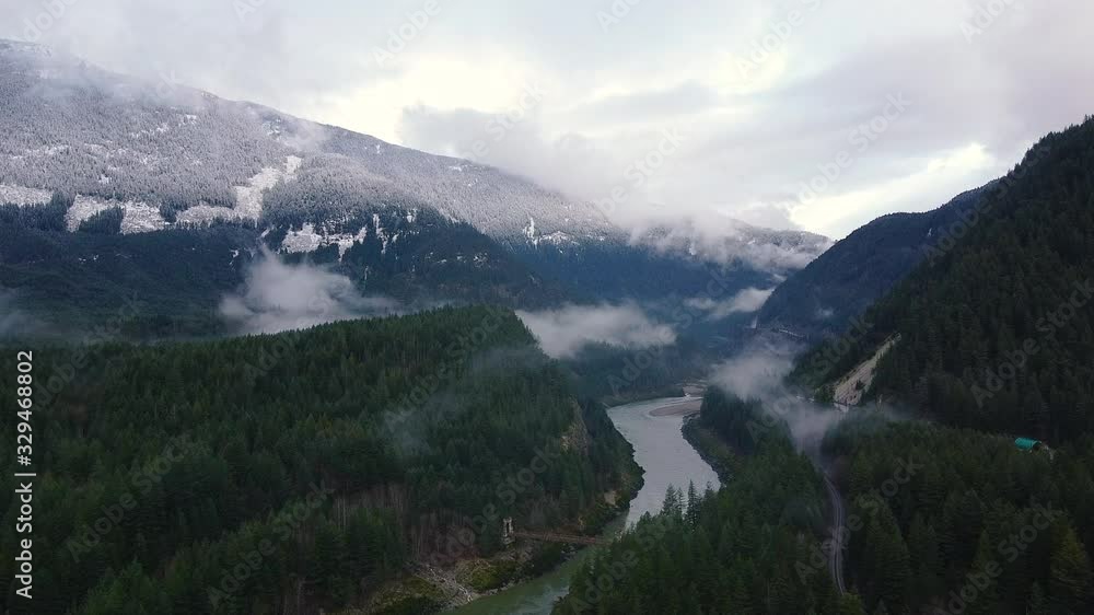Opening shot of the river in valley surround by mountains with green forest and snowy mountaun peaks visible Opening shot of the river in valley surround by mountains with green forest and snowy mountaun peaks visible
