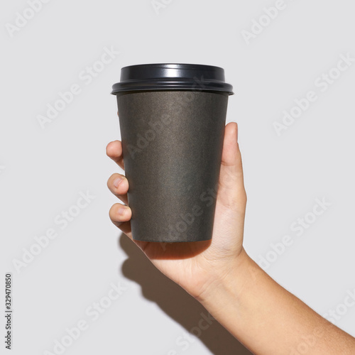Girl hand hold coffee plastic cup. Grey background with copyspace. Female arm holding paper glass. To go, away. No ecology. Hard shadows. Square banner
